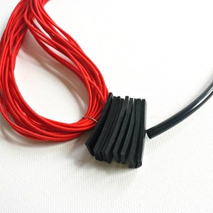 May include: A red cord necklace with a black rubber band accent. The rubber band is made of multiple layers of black rubber.