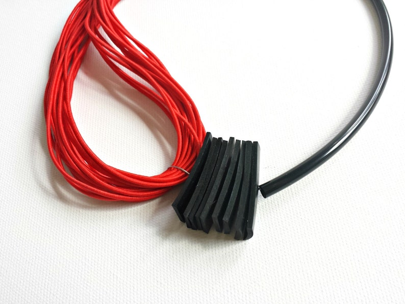 May include: A red cord necklace with a black rubber band accent. The rubber band is made of multiple layers of black rubber.