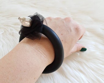 Op de afbeelding: Een zwarte rubberen armband met een grote parel en een zwarte tule bloem accent.