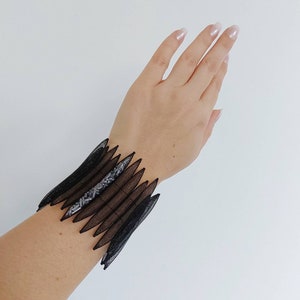 May include: A black mesh bracelet with a geometric design. The bracelet is made of multiple layers of mesh that are layered on top of each other to create a unique and stylish look.