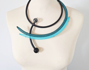 May include: A black and turquoise statement necklace with a geometric design. The necklace features two curved pieces of turquoise mesh and a black band with two black spheres.