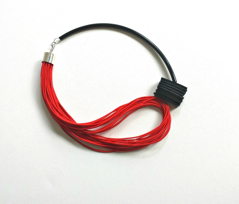 May include: A red and black necklace with a layered, geometric design. The necklace is made of multiple strands of red cord and a black plastic piece.