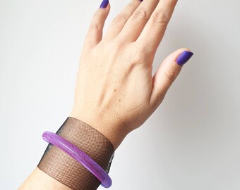 Op de afbeelding: Een paarse en zwarte armband met een gaasontwerp. De armband zit om een pols.