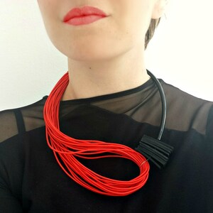 May include: A red and black layered necklace with a geometric design. The necklace is made of thin cords and is worn by a person with red lipstick.