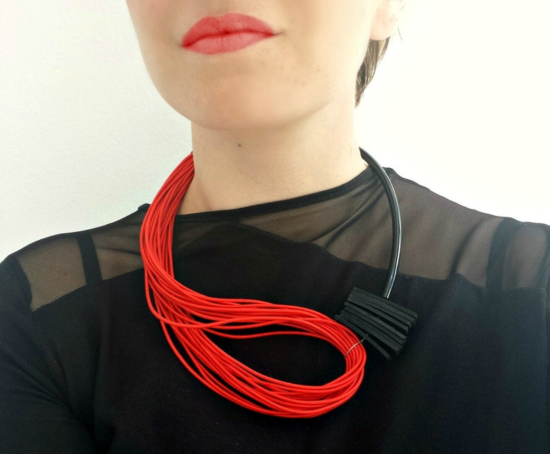 May include: A red and black layered necklace with a geometric design. The necklace is made of thin cords and is worn by a person with red lipstick.