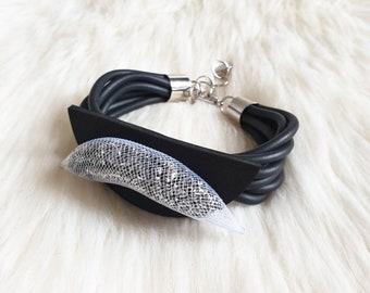 Op de afbeelding: Een zwarte leren armband met een zilveren sluiting en een heldere, glinsterende, halvemaanvormige versiering.