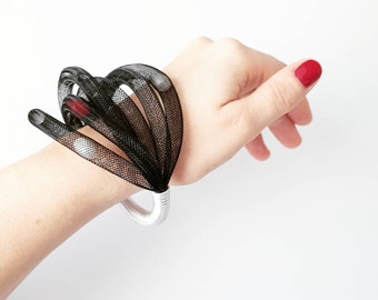 Op de afbeelding: Een zwart-witte mesh armband met een zilveren metalen band. De armband wordt om de pols gedragen.