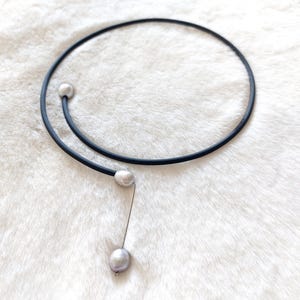May include: A black choker necklace with a single pearl pendant. The necklace is made of a thin, flexible material and has a simple, elegant design.