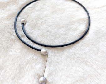 May include: A black choker necklace with a single pearl pendant. The necklace is made of a thin, flexible material and has a simple, elegant design.