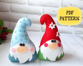 May include: Two felt gnome ornaments, one with a blue hat and the other with a red hat. Both gnomes have white beards, pink cheeks, and black eyes. The text "PDF PATTERN" is in a yellow banner.