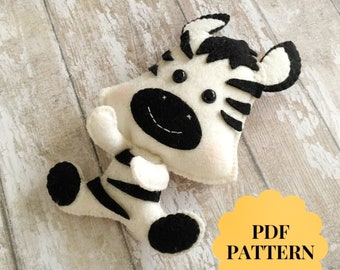 May include: A black and white felt zebra toy with a smiling face. The toy is sitting on a wooden surface. PDF PATTERN.