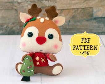 May include: A felt reindeer toy holding a small felt Christmas tree. The reindeer is brown with a red sweater and white snowflakes. The toy is sitting on a white surface. PDF PATTERN + SVG
