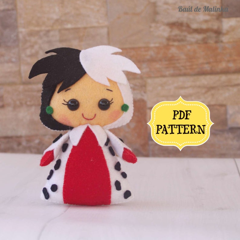 May include: A felt doll of Cruella de Vil from Disney's 101 Dalmatians. The doll is wearing a red and black spotted dress with a white collar. The doll has black and white hair and green eyes. The image also includes the text "PDF PATTERN".