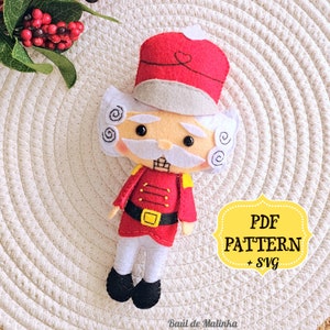 May include: A felt toy nutcracker with a red hat, white beard, and a red and yellow uniform. The toy is on a white background with the text "PDF PATTERN + SVG" in a yellow box.
