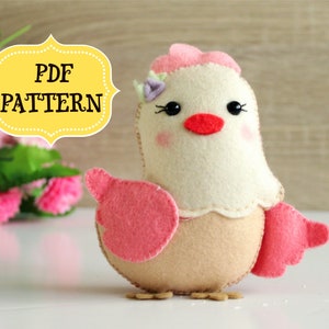 May include: A felt chick toy with pink wings and a pink flower on its head. The chick has black eyes, a red beak, and a beige body. The toy is on a white surface. PDF PATTERN.