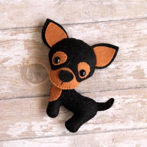 May include: A felt toy dog with brown ears and a black body. The dog has black eyes and a brown nose.
