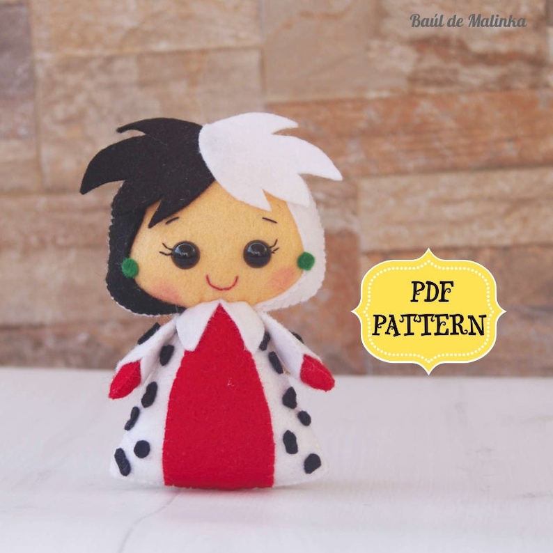 May include: A felt doll of Cruella de Vil from Disney's 101 Dalmatians. The doll is wearing a red and white dress with black spots. The doll has black and white hair and green eyes. The image includes the text "PDF PATTERN".