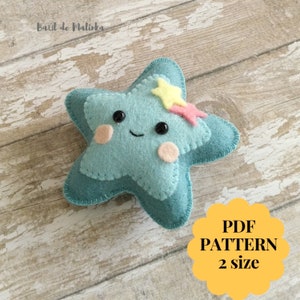 May include: A teal blue felt star with a smiling face, pink cheeks, and black eyes. The star has a yellow and pink star on top. The text "PDF PATTERN 2 size" is on a yellow circle in the bottom right corner of the image.