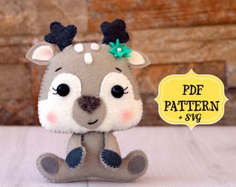 May include: A gray felt deer with a green flower on its head. The deer is sitting with its legs crossed and has black eyes and a pink nose. The image includes the text "PDF PATTERN + SVG".