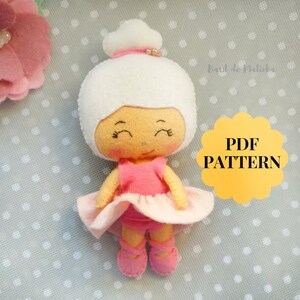 May include: A felt ballerina doll with a white bun, pink tutu, and ballet slippers. The doll has a light skin tone and closed eyes. The image includes a yellow tag with the text "PDF PATTERN".