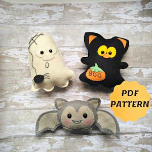 May include: Three handmade Halloween felt decorations: a white ghost with a spider, a black cat with a pumpkin, and a grey bat. The cat has orange ears and eyes. The bat has pink cheeks. The ghost has a stitched face. The image includes the text "PDF PATTERN".