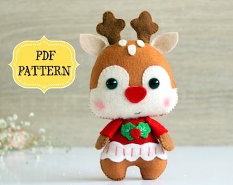 May include: A felt reindeer toy with brown antlers, a red nose, and a red and white dress. The toy is wearing a green holly leaf and berry embellishment on its chest. The text "PDF PATTERN" is on a yellow label in the background.