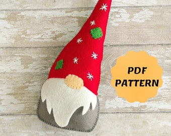 May include: A felt gnome ornament with a red hat, white snowflakes, and green leaves. The gnome has a white beard and a gray base. The text "PDF PATTERN" is on a yellow circle.