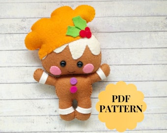 May include: A gingerbread person felt toy pattern in PDF format. The gingerbread person is brown with white icing, pink cheeks, and black eyes. The toy has a green holly leaf and red berry on top of its head. The pattern is available for download.
