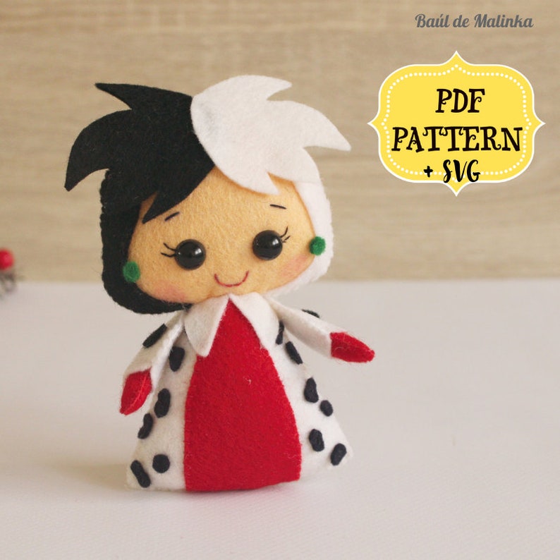 May include: A felt doll of Cruella de Vil from Disney's 101 Dalmatians. The doll is wearing a red dress with black spots and a white and black wig. The doll has a smiling face with green earrings.