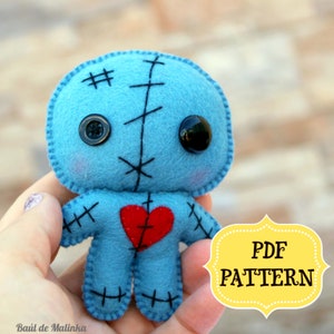 May include: Blue felt voodoo doll with black button eyes, red felt heart, and black stitching.  PDF PATTERN text is in the lower right corner of the image.