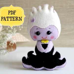 May include: A purple and white felt plush toy of Ursula from The Little Mermaid. The toy is wearing a black dress with a yellow flower on the bodice. The toy has a white crown and purple hair. The toy is sitting on a white surface. The text "PDF PATTERN" is in a yellow banner above the toy.
