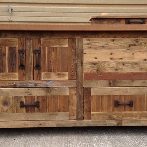 May include: A rustic wooden cabinet with four drawers and two doors. The cabinet is made from reclaimed wood and has a distressed finish. It has metal handles and is on wheels.