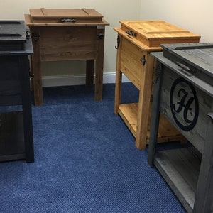 Puede incluir: Cuatro neveras de madera con tapas, dos est&aacute;n te&ntilde;idas de marr&oacute;n oscuro, una est&aacute; te&ntilde;ida de marr&oacute;n claro y una est&aacute; te&ntilde;ida de gris oscuro. La nevera gris tiene un c&iacute;rculo negro con una "H" blanca en el centro. Todas las neveras tienen un estante debajo.