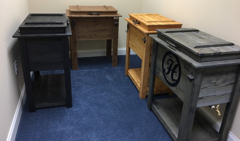 Puede incluir: Cuatro neveras de madera con tapas, dos est&aacute;n te&ntilde;idas de marr&oacute;n oscuro, una est&aacute; te&ntilde;ida de marr&oacute;n claro y una est&aacute; te&ntilde;ida de gris oscuro. La nevera gris tiene un c&iacute;rculo negro con una "H" blanca en el centro. Todas las neveras tienen un estante debajo.