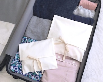 May include: An open suitcase packed with clothes, including a white shirt, a pink shirt, a blue towel, and a floral patterned fabric. The suitcase is lined with a gray mesh fabric and has a black zipper.