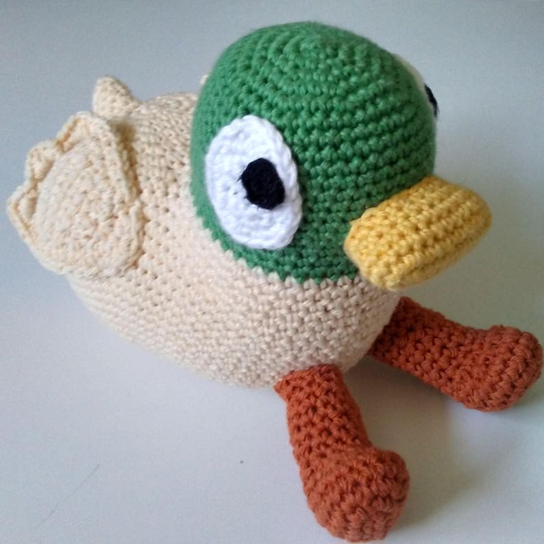 Peut inclure: Un jouet en crochet en forme de canard avec une t&ecirc;te verte, un corps beige, des pattes orange et des yeux noirs.