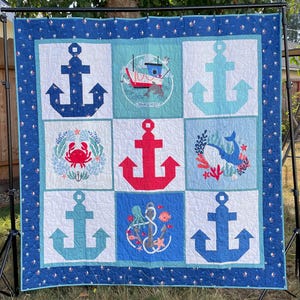 May include: A nautical themed quilt with a blue, red, and white color scheme. The quilt features six squares with anchors, a crab, a fish, an octopus, and a boat. The quilt is made of cotton fabric and is perfect for a nursery or child's room.