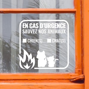 Op de afbeelding: Witte sticker op een raam met de tekst "EN CAS D'URGENCE SAUVEZ NOS ANIMAUX" en vinkjes voor "CHIEN(S)" en "CHAT(S)". Een tekening van een kat en een hond met vlammen eronder.