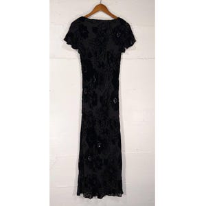 May include: A dark gray, short-sleeved dress with a floral pattern. The dress has a scoop neckline and a fitted silhouette. The floral design is in a darker shade, creating a subtle contrast. The dress is hanging on a wooden hanger.