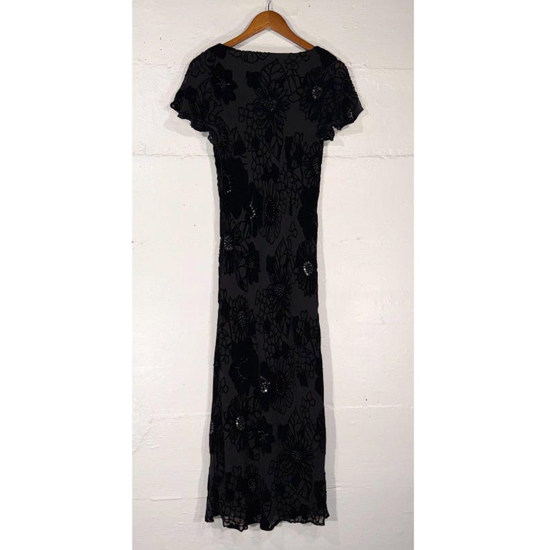 May include: A dark gray, short-sleeved dress with a floral pattern. The dress has a scoop neckline and a fitted silhouette. The floral design is in a darker shade, creating a subtle contrast. The dress is hanging on a wooden hanger.