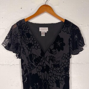 May include: A dark gray dress with a V-neck and short, flutter sleeves. The dress features a floral pattern in a darker shade of gray, with beaded accents. The tag reads "Adrianna Papell."