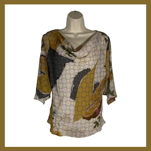 May include: A patterned blouse with a cowl neck and three-quarter sleeves. The top features a mix of colors, including yellow, black, and white, with a floral and geometric design. The blouse is displayed on a mannequin.