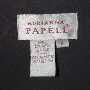 May include: A close-up of a clothing tag from the brand Adrianna Papell. The tag is rectangular with the brand name in a serif font. The tag lists the shell as 72% rayon and 28% silk, with a 100% polyester lining. The size is 6.