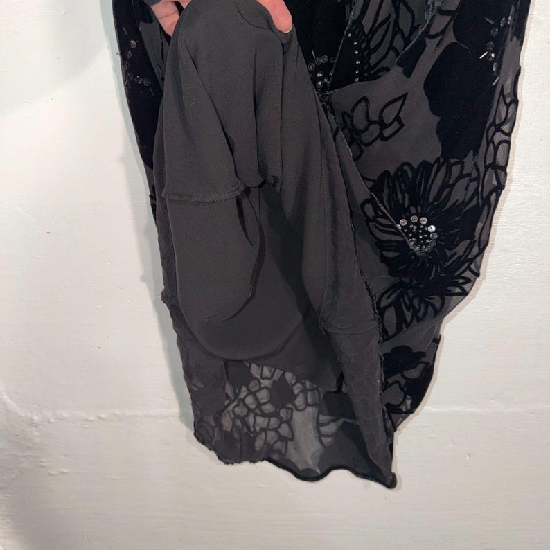 May include: Black dress with a floral pattern. The dress features a dark floral design with sequin accents. The lining is a solid black fabric. The dress is made of a soft, flowing material.
