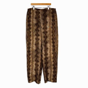 May include: Full-length trousers featuring a brown and black snakeskin print pattern. The pants have a straight-leg silhouette and an elasticized waistband, displayed hanging from a wooden hanger against a plain white background.