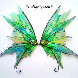 May include: A pair of fairy wings with a green and blue color scheme. The wings have a delicate, translucent appearance with intricate vein detailing. The text "*indigo*moon*" is written at the top of the image. The wings are decorated with gold and jewel accents.