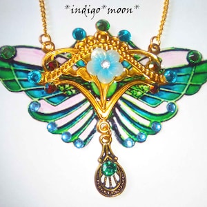May include: A gold butterfly necklace with green and blue enamel wings, a white flower in the center, and a teardrop-shaped pendant.