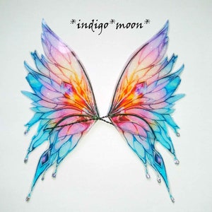 May include: A pair of iridescent fairy wings with a pink, blue and orange colour scheme. The wings are decorated with glitter and have a delicate, ethereal look.