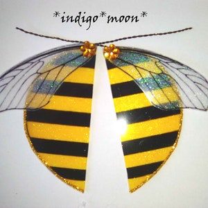 Könnte beinhalten: Ein Paar gelbe und schwarze Bienenflügel mit durchsichtigen, glitzernden Flügeln. Die Flügel sind an einer schwarzen Schnur befestigt.
