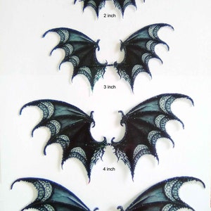 Pode incluir: Cinco pares de asas de renda preta e branca com glitter. As asas estão disponíveis em cinco tamanhos: 1 polegada, 2 polegadas, 3 polegadas, 4 polegadas e 5 polegadas. *indigo*moon* está escrito no topo da imagem.